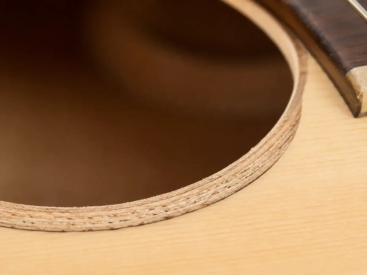 Soundhole edge of a laminate acoustic guitar showing distinct plywood-like layers