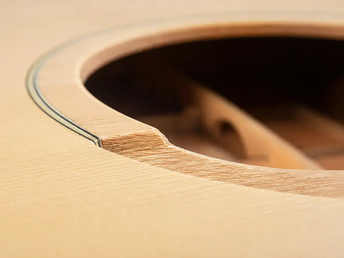 Soundhole edge of a solid-wood acoustic guitar showing continuous grain through the full thickness